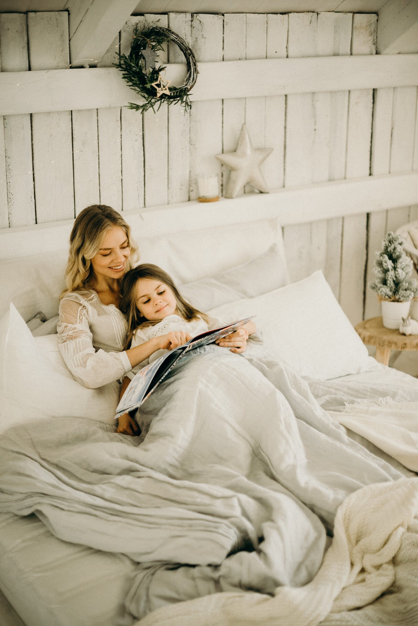Mother and daughter snuggling reading a book in bed.